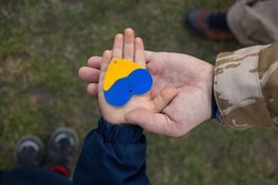hand of a child in the hand of a man in camouflage with a yellow and blue heart. Family, patriotism, unity, support. Russia's invasion of Ukraine, a request for help to the world community