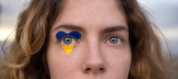 female eyes close-up with a drawn flag of Ukraine. National symbol of freedom and independence. Russian invasion of Ukraine, Stop the war. Hope and Faith