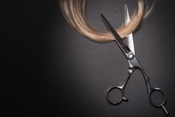 Scissors and piece of blond hair. Professional barber hair cutting shears on black background. Hairdresser salon equipment concept, premium hairdressing set. Accessories for haircut with copy space
