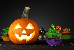 Halloween cupcake. Pumpkin Jack o lantern. Dessert on Halloween party. Muffin decorated with colored frosting and Icing shaped pumpkin Jack-o-lantern. Cupcakes on wooden black background. High quality
