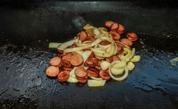 Polska kielbasa sausage and sautéed onions cooking on the black stone griddle