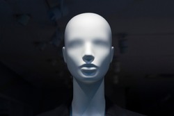 A close-up of a mannequin’s head in a window of a mall on the dark background with switched off electric lamps on the ceiling. Copy space.