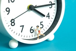 Miniature people toy figure photography. Running daily routine concept. A young girl runner jogging above clock, isolated on blue background. Image photo
