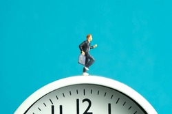 Miniature people toy figure photography. End and start of school concept. Young men pupil running above white clock isolated on blue background. Image photo