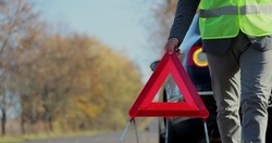 Close up hand of man putting warning triangle by the broken car on a road. Concept road accident. Help repair.