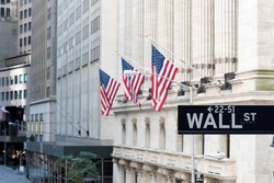 Wall Street sign with american flags and New York Stock Exchange in New York City.