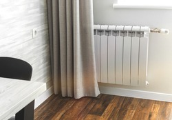 Heating metal radiator, white radiator in a modern apartment interior with wooden floor