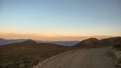 A graded dirt road cuts through high desert mountains headed east.