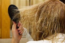 blond combing wet and tangled hair. Young woman combing her tangled hair after shower, close-up.