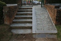 Steps, a staircase with handrails, railings, descent and ascent for people with disabilities and prams, bicycles. Made from stone cemented. Brick wall on the side.