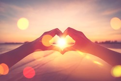 Female hands heart shape on nature bokeh sun light flare wave and blur tropical sunset beach abstract background. Copy space of happy love travel and freedom in nature concept. Vintage tone color.
