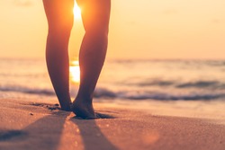 Close up woman legs walking on tropical sunset beach with smooth wave and bokeh sun light wave abstract background. Travel vacation and freedom feel good concept. Vintage tone filter color style.