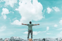 Man raise hand up at top of rock on blue sky and white cloud abstract background. Freedom feel good and travel adventure vacation concept. Vintage tone filter effect color style.