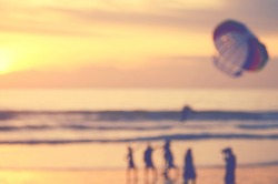 Blur people relax on tropical sunset beach with parachuting boat abstract background.Travel concept.Retro color style.