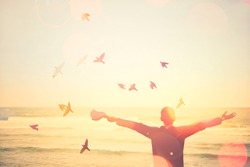 freedom and feel good concept. Man rising hand at sunset beach with birds fly and colorful bokeh light abstract texture background. Vintage tone color style.