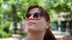 Awesome young caucasian woman lookingup in park with cool reflection in her sunglasses. Bright Sunny day in summer.