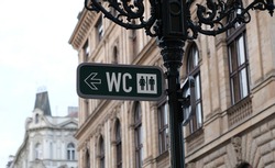 WC sign, logo of public toilets in the street against building background. For female, male. Public toilet sign on vintage street light pillar. Street lamp with wc symbols in downtown Prague. 