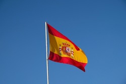 Spanish national flag waving on blue sky background. The flag on a flagpole flutters in the wind. Red with yellow Spain Flag blowing in the wind against on blue sky