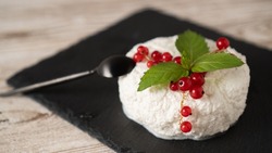 White cottage cheese on a black plate with mint and red currants. Ricotta cheese with red berry on black background