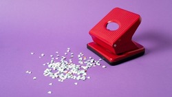 Red confetti maker. Hole puncher machine. Paper punch sprinkle. Hole punch art. Red puncher on violet background