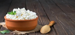 Farmer's cottage cheese in a traditional clay bowl, next to a wooden spoon, a dark wooden background. Close-up, selective focus. Soft curd natural healthy food, wholesome diet food