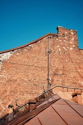 Wall of an old brick house and an old metal roof with antennas, details of medieval city against the blue sky. Journey through old cities, background idea for advertising or travel description