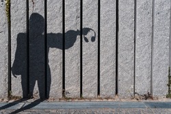 Rare view of shadow silhouette of a woman in the city street holding headphones with hand in sunny day. Concept of emotions and social issues. Copy space for text
