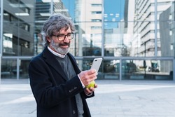 Modern mature businessman using mobile phone outside office building