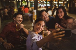 Asian friends Drinking beer outdoors at the brewery for the New Year festival.She is taking a selfie night time