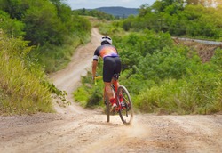 Asian man riding a bicycle on gravel road, he brakes down a hill.