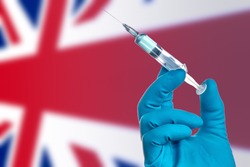  Fight against the epidemic of coronavirus in Great Britain.Doctor's hand in medical gloves with vaccine for  COVID-19 on the background of the flag Great Britain. Flu shot  in Great Britain