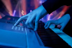 close-up of the hands of a musician playing a synthesizer against the backdrop of concert spotlights