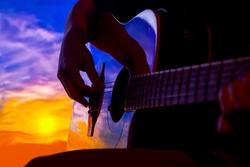 silhouette hand of musician playing acoustic guitar at sunset