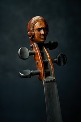 Very old, antique, classical violin with a wood carved headstock, portrait of a nobleman in a wig. A bit dusty, wooden instrument hand made in Europe. High resolution and precision photo for poster