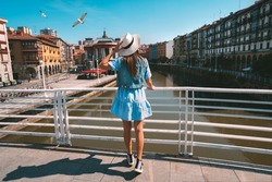 Rear view of young tourist woman in white sun hat walking in Bilbao city. Summer holiday vacation in Spain