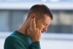 Man with tinnitus. Man touching his ear because of strong earache or ear pain. Otitis
