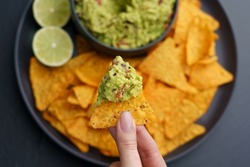 Top view of woman hand holding tortilla chips or nachos with tasty guacamole dip