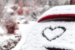 Heart shape drawn by hand on car window covered with fresh snow. Frozen rear windshield with heart on winter day