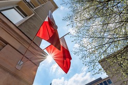 Flag of Poland on facade of a building waving in the wind with sun rays. Celebrating Polish National Flag Day
