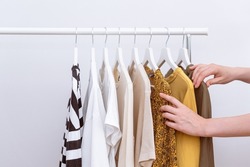 Woman choosing and picking out clothes to buy hanging on clothing rack in fashion store, close up of hands. Female clothes organized on clothes hangers. Shopping concept