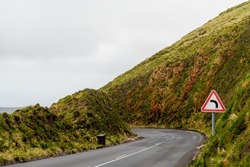 Mountain winding road and green hills. Warning sign of sharp turn left on the road ahead near an empty asphalt road