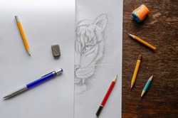 Monochrome Drawing of a tiger made by a pencil on a white sheet of paper. Half of the drawing is covered with a blank sheet of paper. Drawing training, creativity. Top view at an angle.