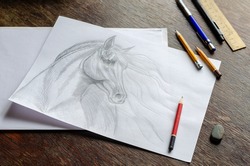 Horse portrait drawn in pencil on white paper. Monochrome drawing of an animal with a long mane on a brown wooden table. Pencils, eraser and ruler. Art, hobby, recreation. Artist talent. Indoors.