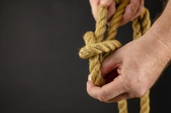 An adult male is spooling rope against black background. Hands untie knots on yellow burlap rope. Close-up. Selective Focus.