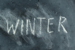 Semi-erased word WINTER on black chalkboard. Handwritten word. Fuzzy letters on black surface. The concept of the changing seasons of the year.