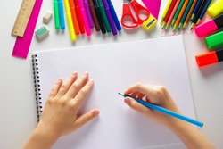blue pencil in children's hands and a white notebook. background of pencils, felt-tip pens
