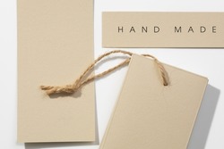 Three cardboard rectangular brand tags of gray-brown color with inscription on top right label saying item is hand made and rope on bottom right one put on white background. Tag mock up. Copy space.