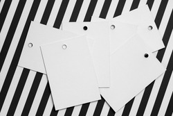 Stack of white cardboard label tags for clothes with little holes in top part of each positioned in center on zebra-like white and black background. Tag mock up. Copy space.
