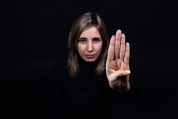Young woman asking for help from domestic assault and abuse by showing stop sign with hand looking at camera on black background. Relative aggression. Gaslighting.