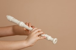 Hold fipple flute with both hands and pinch holes closeup, beige background. Woodwind musical instrument. Aerophone or reedless wind instrument that produce sound from flow of air across opening.